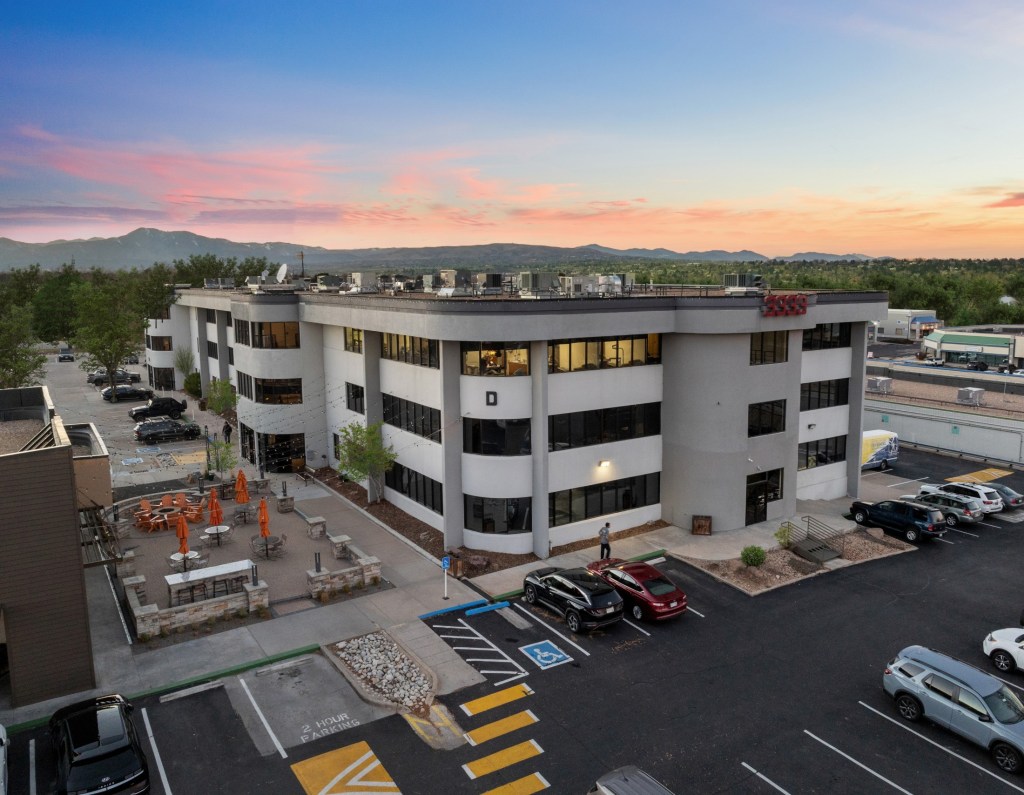 Two-story white office building at dusk; parking lot, landscaping, and mountains in background