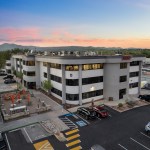 Two-story white office building at dusk; parking lot, landscaping, and mountains in background